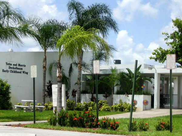 An image of a white building, with palm trees in the front, and clouds overhead, showcasing a job well done by Rainbow Painting Contractor Davie.